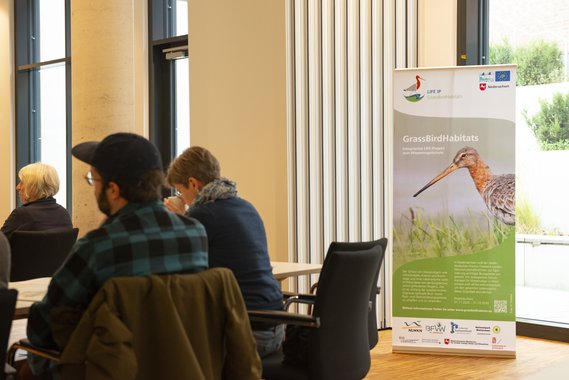People sitting in front of information roll-ups of the project LIFE IP GrassBirdHabitats.